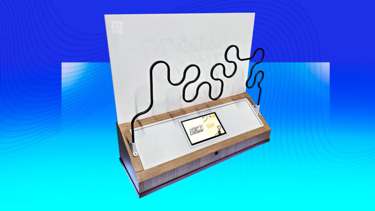 Modelo de mesa do labirinto elétrico, com estrutura em acabamento de madeira, tela digital na base e uma barra metálica com curvas acentuadas.